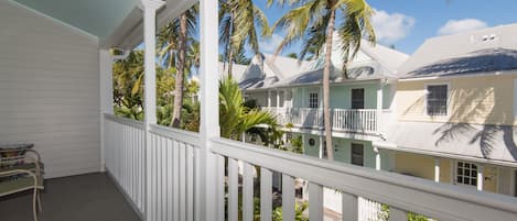 A covered porch with a white railing, overlooking a residential area with houses and palm trees.