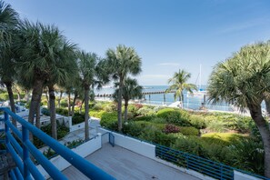 A balcony with blue railings overlooking a landscaped garden with palm trees and a view of the sea.