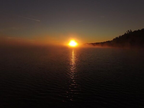 A sunset over a calm body of water with a silhouette of a forested hill in the background.