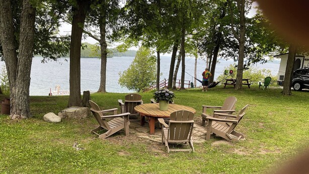 Zona salotto all'aperto sul lago, con un tavolo di legno rotondo e quattro poltrone Adirondack.