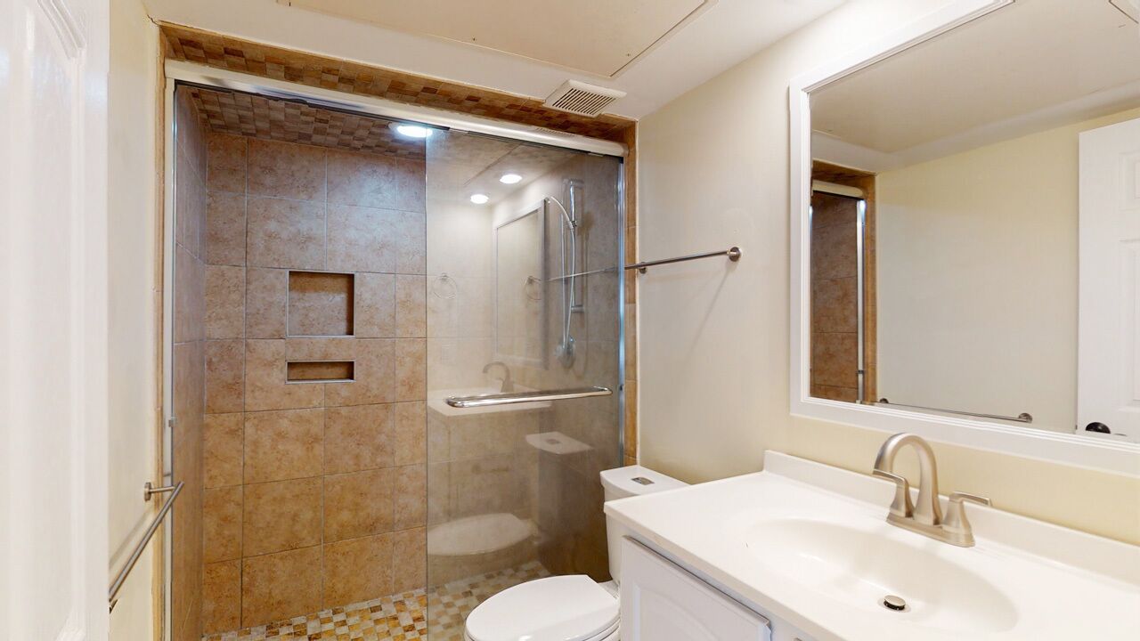Un baño con ducha de vidrio, un lavamanos blanco y un espejo grande.