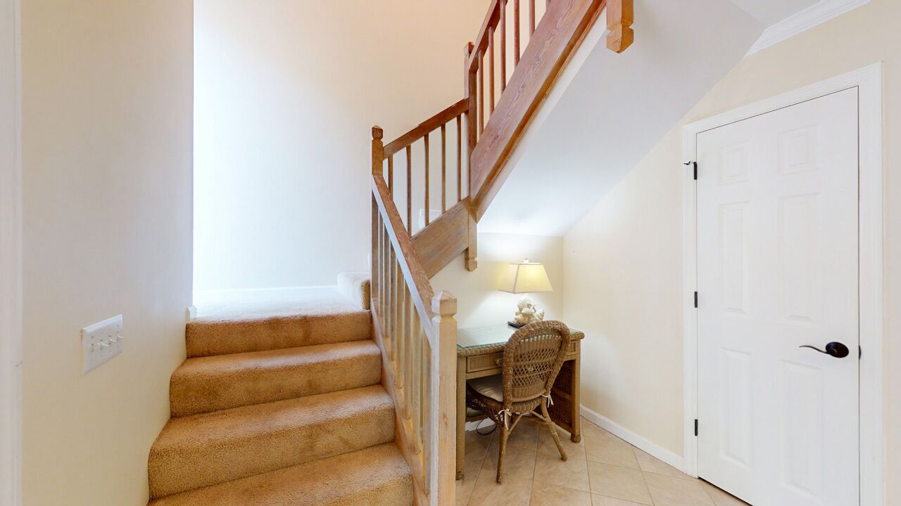 A staircase with wooden railings leading to a landing. There is a desk with a chair and a lamp on the landing.
