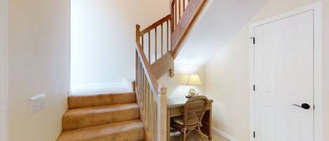 A staircase with wooden railings leading to a landing. There is a desk with a chair and a lamp on the landing.