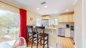 A kitchen with wooden cabinets, a stainless steel refrigerator, and a bar area with two chairs. - Very peaceful and tranquil setting. (Hilton Head)