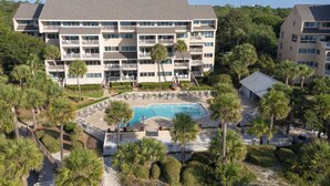 A multi-story hotel with a swimming pool surrounded by palm trees and a well-maintained lawn.