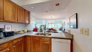 A modern kitchen with wooden cabinets, granite countertops, a built-in dishwasher, and a dining area with a red sofa and chandelier.