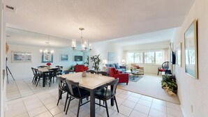 A spacious living area with a dining table, chairs, a red sofa, and a TV mounted on the wall.