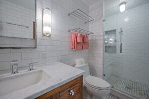 A bathroom with a marble sink, white tiled walls, a glass shower enclosure, and a toilet.