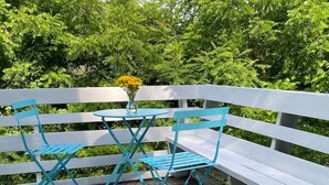 Una terraza con barandilla blanca, dos sillas azules y una pequeña mesa redonda con un florero de flores amarillas.
