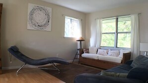 Una sala de estar con una chaise longue, un sofá, una lámpara de pie y una ventana con cortinas.