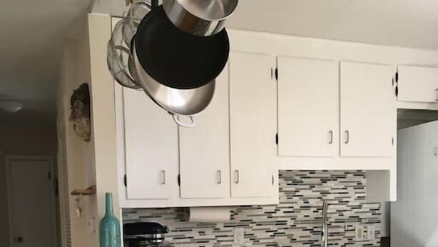 Una cocina con armarios blancos, salpicadero de azulejos y una estufa a gas.