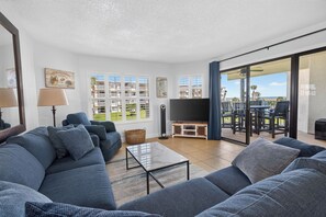 A living room with a sofa set, a television, and a view of the outdoors through a sliding glass door.