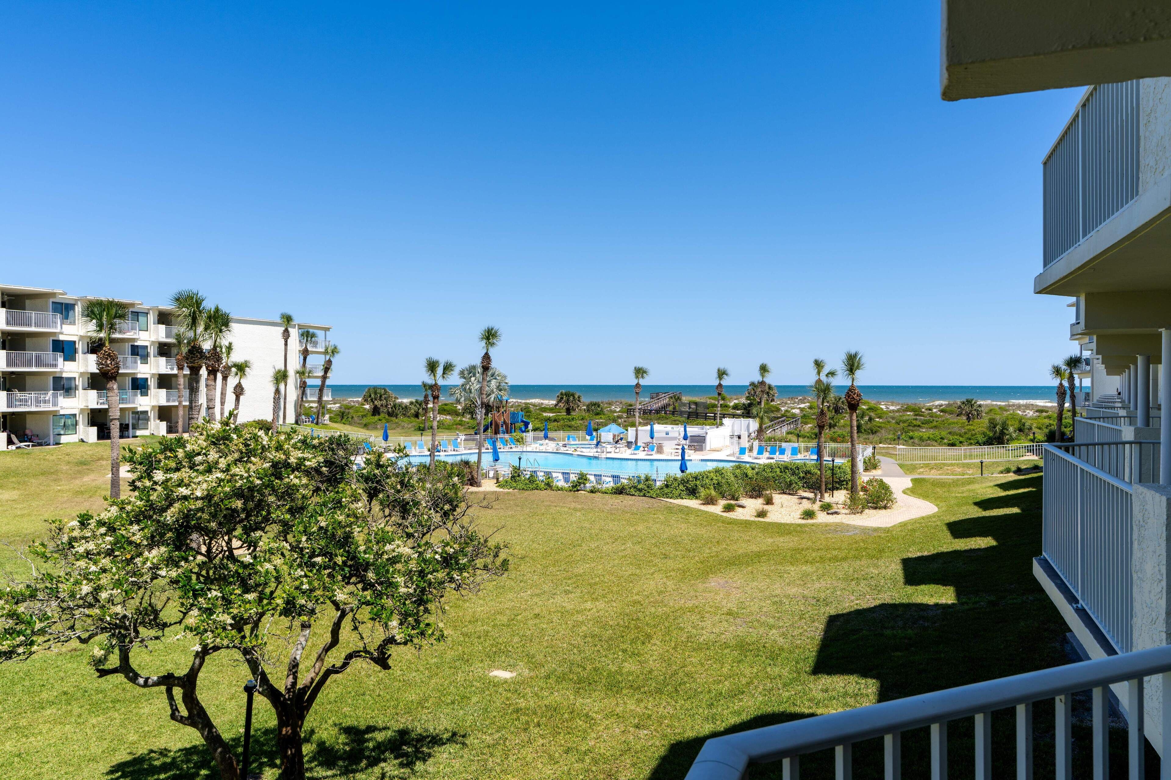 A resort with a pool area, palm trees, and a view of the ocean.