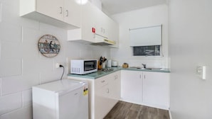 Une cuisine compacte avec des meubles blancs, un four à micro-ondes, un petit réfrigérateur et une fenêtre donnant sur un beau paysage.