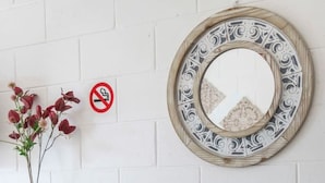 Une table blanche avec deux chaises, un miroir décoratif, un panneau «interdiction de fumer» et un vase rempli de fleurs.