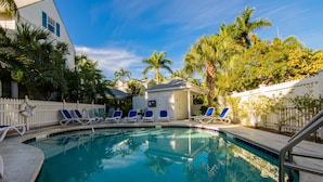 A swimming pool with lounge chairs and a small building, surrounded by palm trees and a white picket fence. - Life in the Slow Lane at the Truman Annex in Key West (Key West)