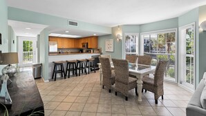 A spacious kitchen with wooden cabinets, a central island, and a dining area with wicker chairs. - Updated 2 BR! Breathtaking View of the Gulf Sunsets! B1113A (Cape Haze)