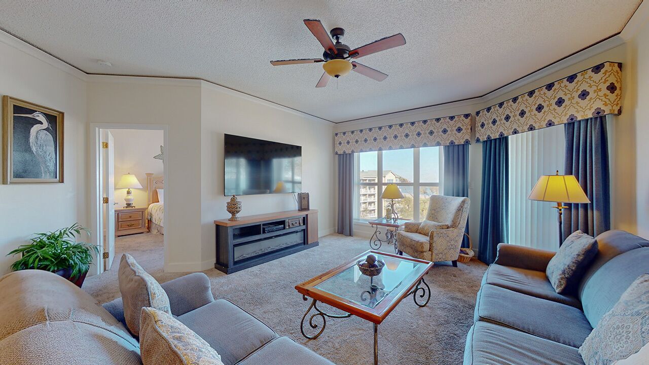 A living room with a ceiling fan, a TV, a sofa, a coffee table, and a window with curtains.