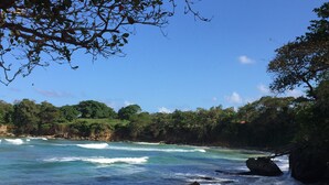 A beach with clear turquoise water, rocky outcrops, and dense green foliage in the background.
