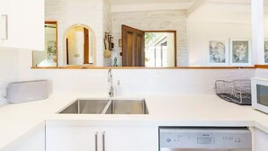 A modern kitchen with white cabinetry, a stainless steel sink, and a built-in dishwasher. - AZURE - BEACH HOUSE ON THE BEACH (Marcus Beach)