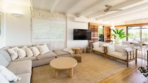 A modern living room with a large sectional sofa, a round coffee table, and a flat-screen TV mounted on the wall. - AZURE - BEACH HOUSE ON THE BEACH (Marcus Beach)