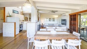 A spacious living area with a wooden dining table, white chairs, a sofa, and a television. - AZURE - BEACH HOUSE ON THE BEACH (Marcus Beach)