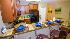A kitchen with wooden cabinets, a black refrigerator, a granite countertop, and bar stools. - Executive 5 Bed 4.5 Bath Vacation Home W/ Pool, Spa Near Disney  (Kissimmee)