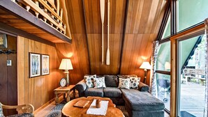 A cozy cabin interior with a wooden ceiling, a sofa set, a coffee table, and a view of the outdoors through large windows. - Serene Washington Escape w/ Deck & Mountain Views! (Packwood)