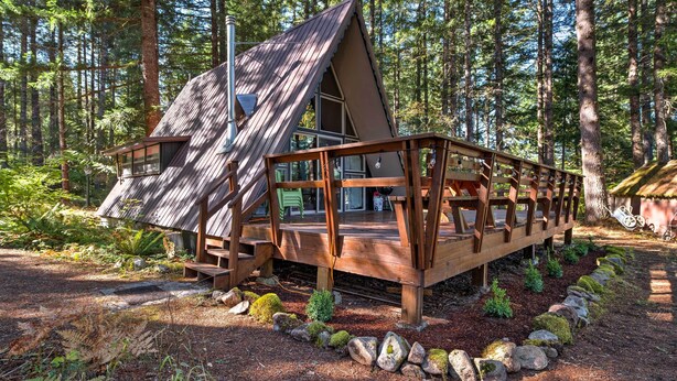 A cabin with a sloped roof, wooden deck, and a small porch. - Serene Washington Escape w/ Deck & Mountain Views! (Packwood)