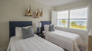 A hotel room with two beds, a large window with a view of the ocean, and a ceiling fan.