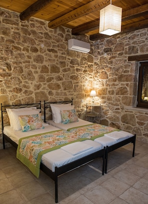 A stone-walled bedroom with a bed, pillows, a bedside table with a lamp, and a hanging light fixture.