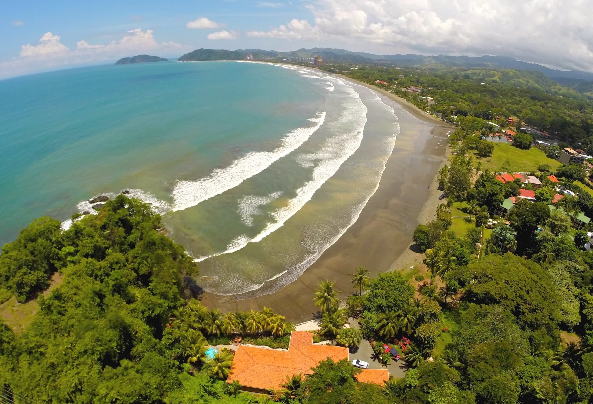 Vista aérea de una zona costera con playa, abundante vegetación y cielo despejado.