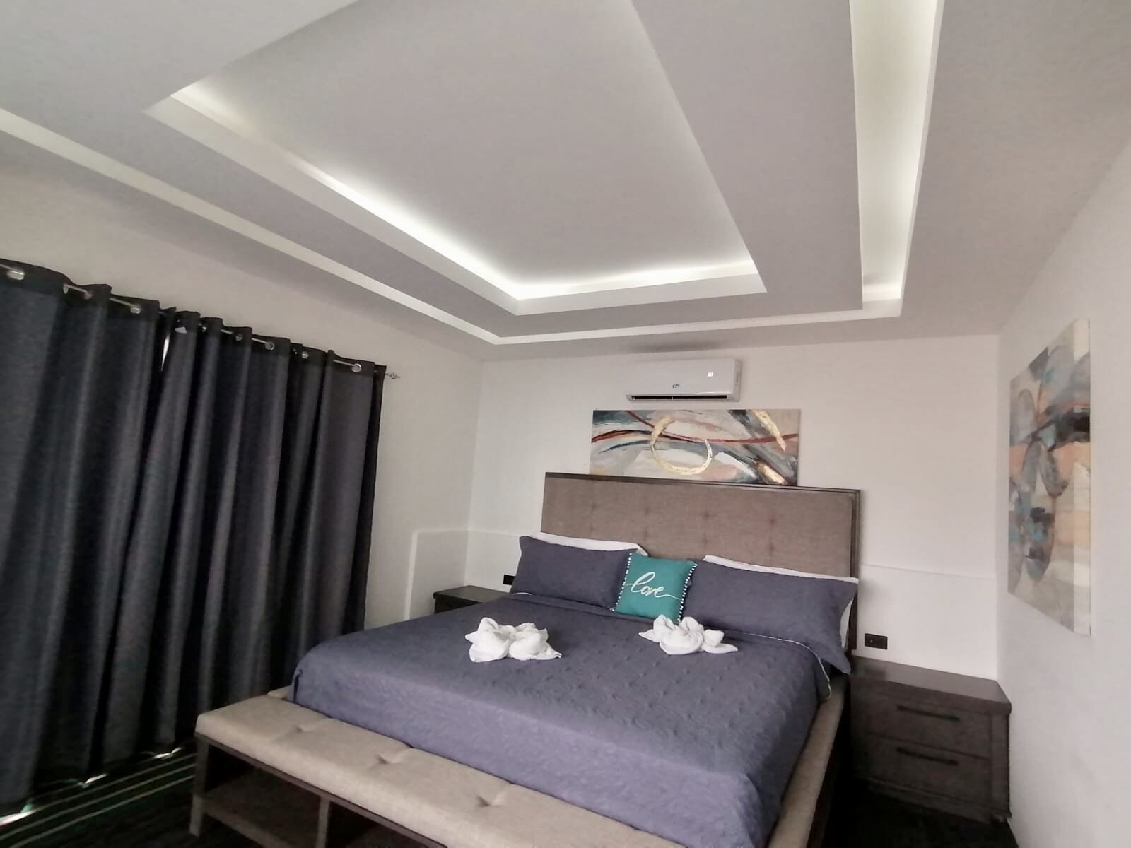 Une chambre à coucher moderne, comprenant un lit, des tables de chevet, un banc et un luminaire fixé au plafond.