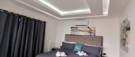 Une chambre à coucher moderne, comprenant un lit, des tables de chevet, un banc et un luminaire fixé au plafond.