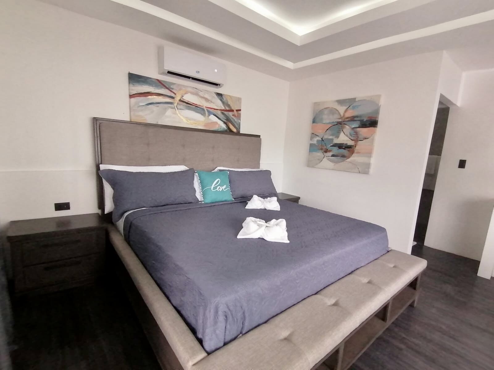 A modern bedroom with a large bed, a bench at the foot, and two paintings on the walls.