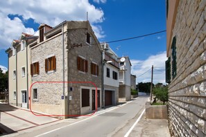Vista de una calle con un edificio de piedra, cielo despejado y una carretera visible.