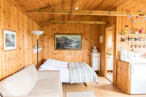 Een houten kamer met een bed, een slaapbank, een schilderij, een lamp en een kitchenette.