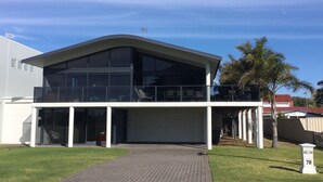 A modern two-story house with a large glass balcony, a garage, and a well-maintained lawn.