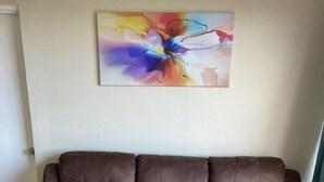 Een bruine leren bank met een geborduurde rugleuning en armleuningen, geplaatst in een kamer met een marmeren vloer en een kleurrijk abstract schilderij aan de muur.