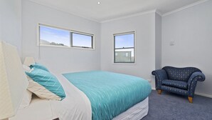 Un dormitorio con una cama, dos ventanas, una silla y piso alfombrado.