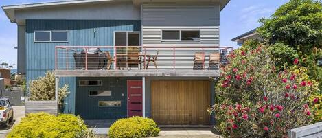 Une maison moderne à deux étages, dotée d’un balcon, d’un garage et d’un jardin bien entretenu.