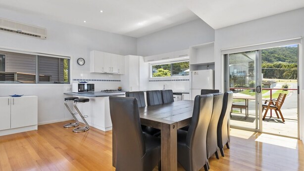 Una cocina moderna con armarios blancos, un comedor con mesa y sillas de madera, y vistas al verdor a través de amplios ventanales.