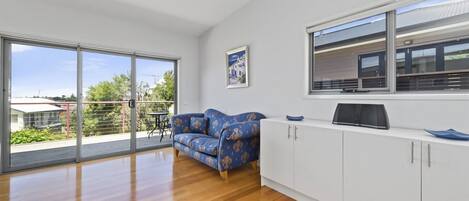 A spacious living area with a large sliding glass door leading to a balcony, a blue patterned sofa, a white cabinet, and a framed picture on the wall.
