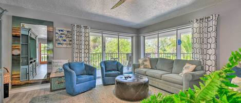 A spacious living room with a ceiling fan, large windows, a gray sofa, blue armchairs, and a coffee table.