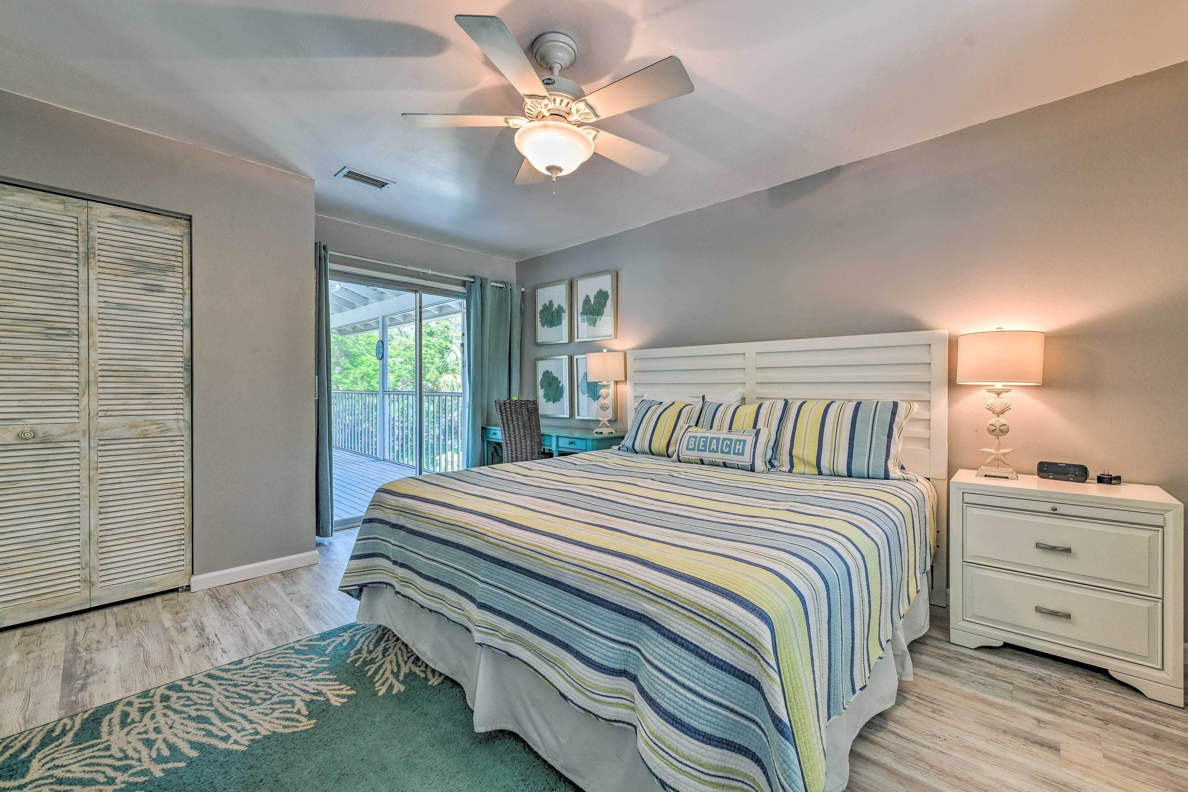 A bedroom with a bed, nightstands, a ceiling fan, and a view of the outdoors.
