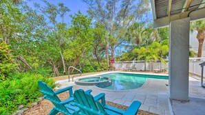 Un patio trasero con piscina, sillas Adirondack verdes y una cerca blanca.