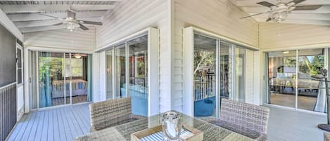 A covered outdoor area with a table and chairs, a ceiling fan, and a view of the backyard through glass doors.