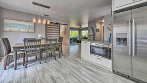 Una cocina moderna con refrigerador de acero inoxidable, mesa de comedor de madera y lámparas colgantes.
