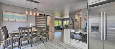 A modern kitchen with a stainless steel refrigerator, wooden dining table, and hanging pendant lights.