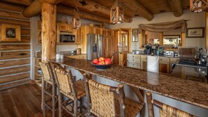A rustic kitchen with wooden beams, a granite countertop, and a central island with bar stools. - Enchanting Private Mountain Sanctuary! Spectacular Views (Big Sky)